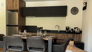 Una cocina moderna con zona de comedor, que incluye un sofá con un cojín mullido, una mesa dispuesta con vasos y un refrigerador.