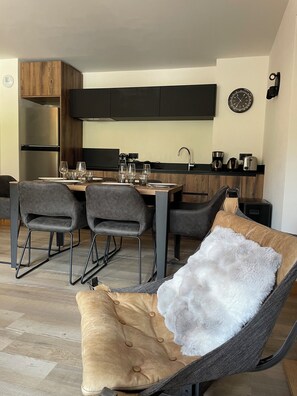 Eine moderne Küche mit Essbereich, inklusive einer Couch mit einem flauschigen Kissen, einem Tisch gedeckt mit Gläsern und einem Kühlschrank.