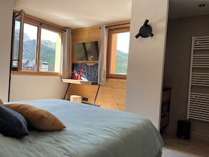 Un dormitori amb un llit, un televisor fixat a una paret de fusta, una finestra amb cortines i vistes a les muntanyes.