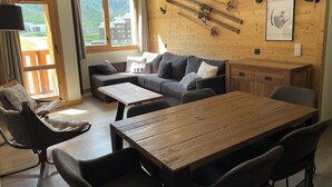 Una habitación acogedora con una mesa de madera, un sofá y una silla. Se observan esquíes montados en la pared y un cartel.