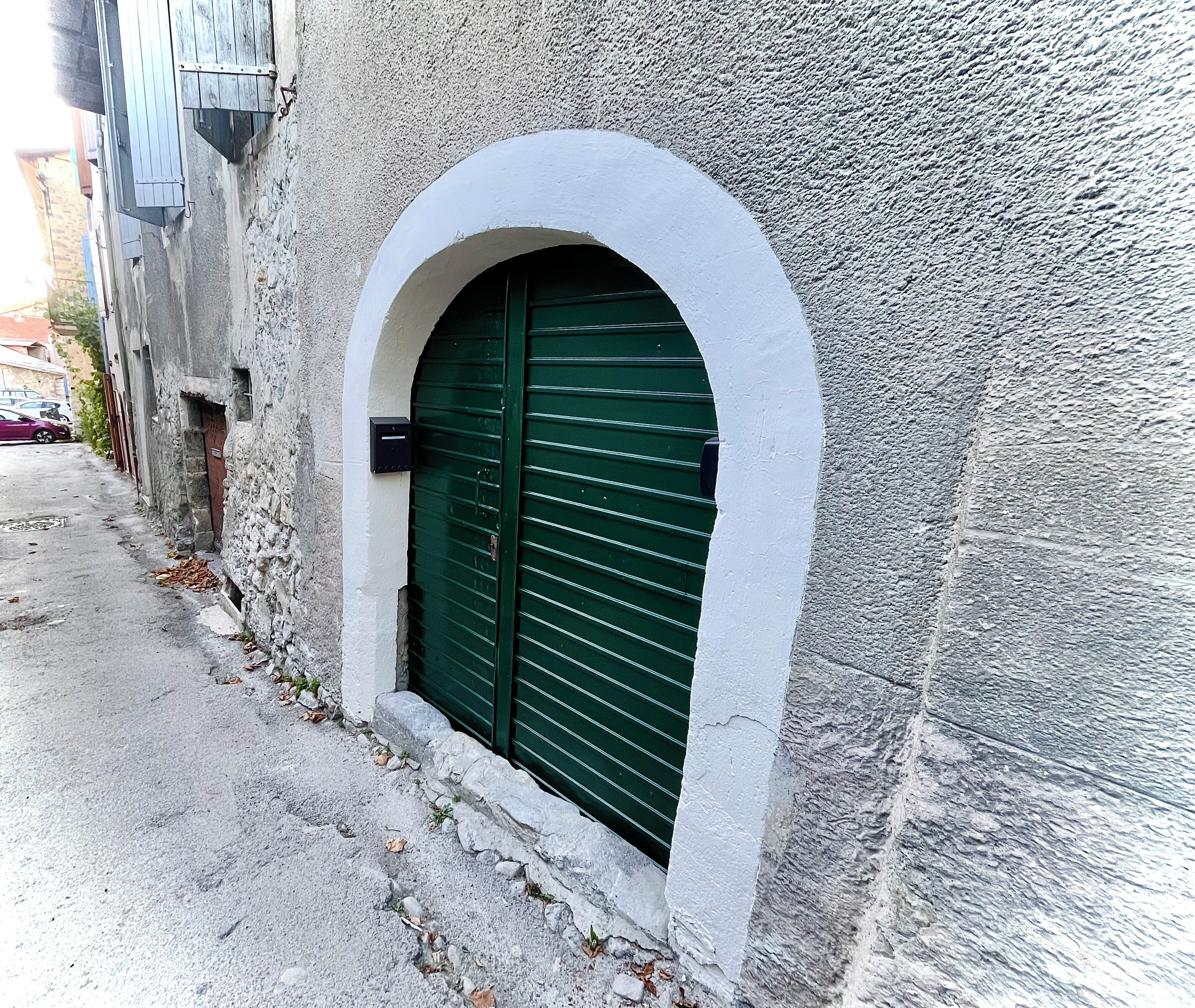 Un edificio con una entrada con persianas verdes, un ventanal arqueado blanco y una pared de piedra texturizada.