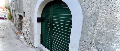 Un edificio con una entrada con persianas verdes, un ventanal arqueado blanco y una pared de piedra texturizada.