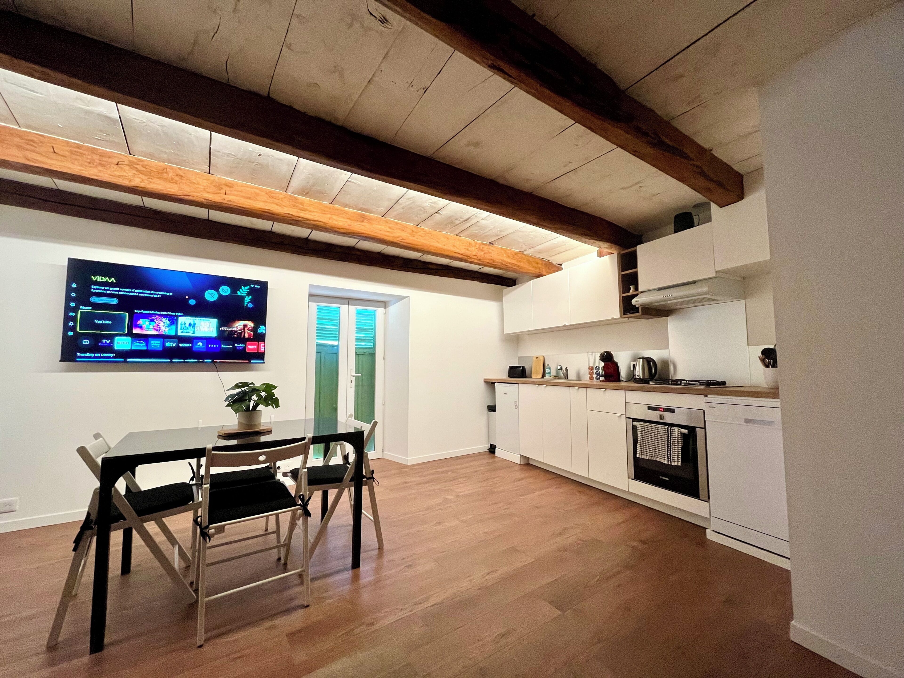 Una cocina moderna con armarios blancos, techo de madera y comedor con mesa y sillas.