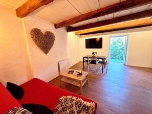 A living room with a red sofa, a wooden coffee table, a heart-shaped wall decoration, a dining area with a table and chairs, and a TV mounted on the wall. - Cozy apartment in the heart of Veynes with a balcony and a view of the mountains 🏔️ (Veynes)