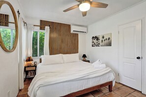 A bedroom with a bed, a ceiling fan, an air conditioning unit, a bedside table with a lamp, a wall-mounted picture, and a door. - Sunny Regards Retreat (Fort Lauderdale)