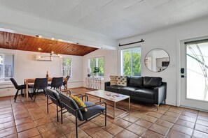 A modern living room with a dining area, a sofa, a coffee table, and a large window providing natural light. - Sunny Regards Retreat (Fort Lauderdale)