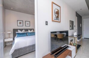 Ein modernes Hotelzimmer mit Bett, Nachttisch, Lampe, Kunstwerk und Fernseher.