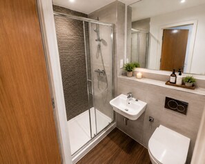 Un baño moderno con ducha envuelta en vidrio, un lavamanos blanco y un inodoro.
