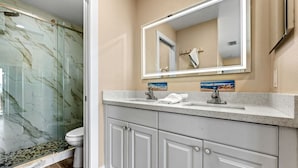 A bathroom with a glass shower enclosure, a white toilet, a vanity with a mirror, and a sink.