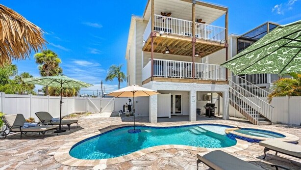 A two-story building with a swimming pool, outdoor seating, and a covered area with umbrellas.