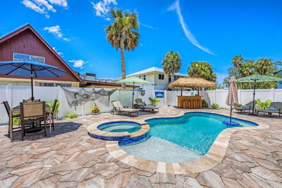 A backyard with a swimming pool, lounge chairs, and a thatched-roof structure.