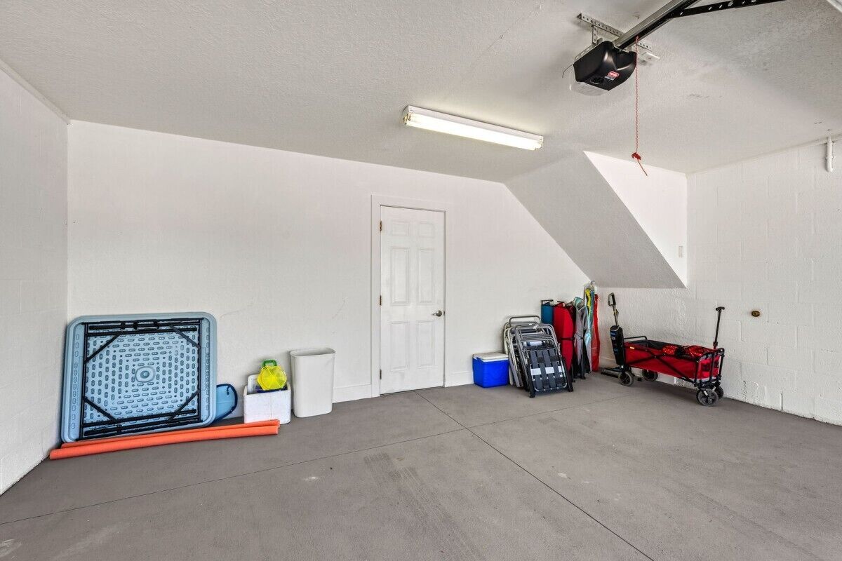 A garage with a sloped ceiling, a white door, and various items including a blue cooler, a red cart, and a black toolbox.