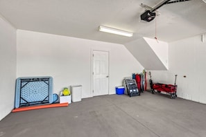 A garage with a sloped ceiling, a white door, and various items including a blue cooler, a red cart, and a black toolbox.