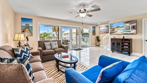 A spacious living area with a ceiling fan, a blue sofa, a brown sofa, a coffee table, and a bookshelf.