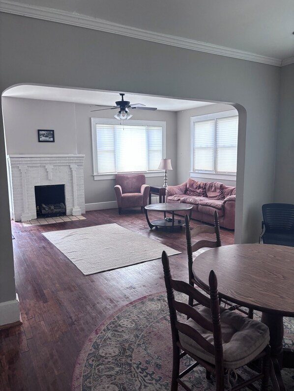 A living room with a fireplace, a ceiling fan, a sofa, a coffee table, and a dining table with chairs.