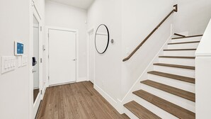 A modern interior with a wooden staircase, white walls, and a door with a digital display. - New Build Near Downtown + Balcony + Backyard (Houston)