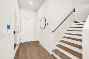 Ein modernes Interieur mit einer Holztreppe, weißen Wänden und einer Tür mit digitaler Anzeige.