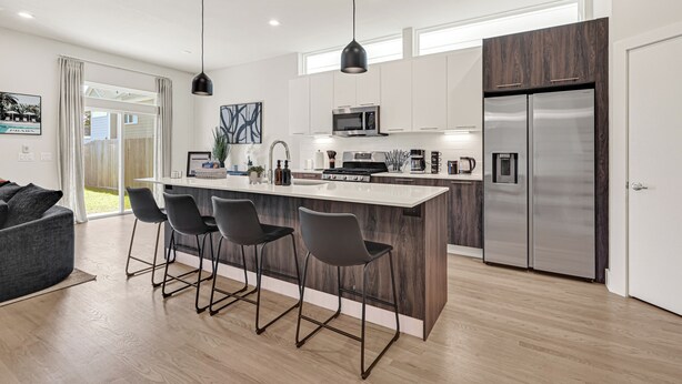 A modern kitchen with a central island, bar stools, a refrigerator, and a dining area with a sofa. - New Build Near Downtown + Balcony + Backyard (Houston)