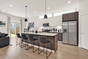 Una cocina moderna con una isla central, taburetes de bar, un refrigerador y un comedor con sofá.