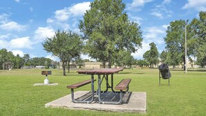 A picnic table with benches in a grassy park area with trees and a building in the background. - New Build Near Downtown + Balcony + Backyard (Houston)