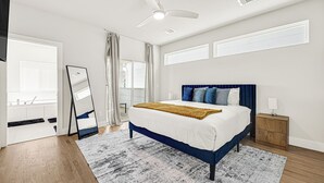 A bedroom with a bed, a nightstand, a mirror, a ceiling fan, and a window with curtains. - New Build Near Downtown + Balcony + Backyard (Houston)