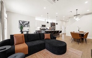 Un área de estar moderna con un sofá modular, una mesa de comedor con sillas y una cocina al fondo.