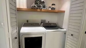 Een wasserette met twee gestapelde wasmachines en drogers, een plank erboven en een deur aan de linkerkant.