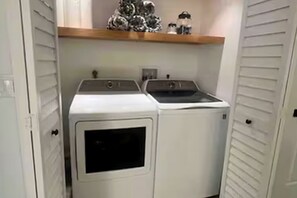 A laundry room with two stacked washers and dryers, a shelf above, and a door on the left. - Your Beachfront Escap: Spacious 3 Bedroom 2 bath Condo in Ponce Inlet, Florida (Ponce Inlet)