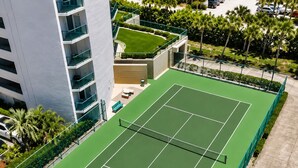 Luchtbeeld van een tennisbaan omringd door een groene hekken, met een gebouw ernaast.