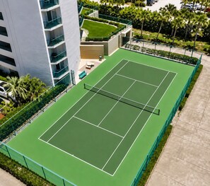 An aerial view of a tennis court surrounded by a green fence, with a building adjacent to it. - Your Beachfront Escap: Spacious 3 Bedroom 2 bath Condo in Ponce Inlet, Florida (Ponce Inlet)