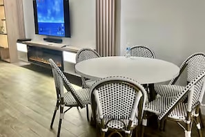Mesa de jantar redonda com quatro cadeiras de vime, televisão de tela plana na parede e lareira embutida.