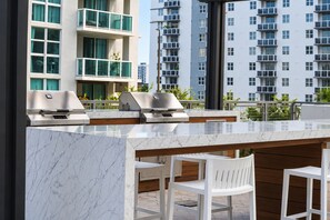 An outdoor bar area with a marble countertop, two built-in grills, and white chairs. - 2 Bed Apartment Miami Wynwood Design District Full Amenities (Miami)