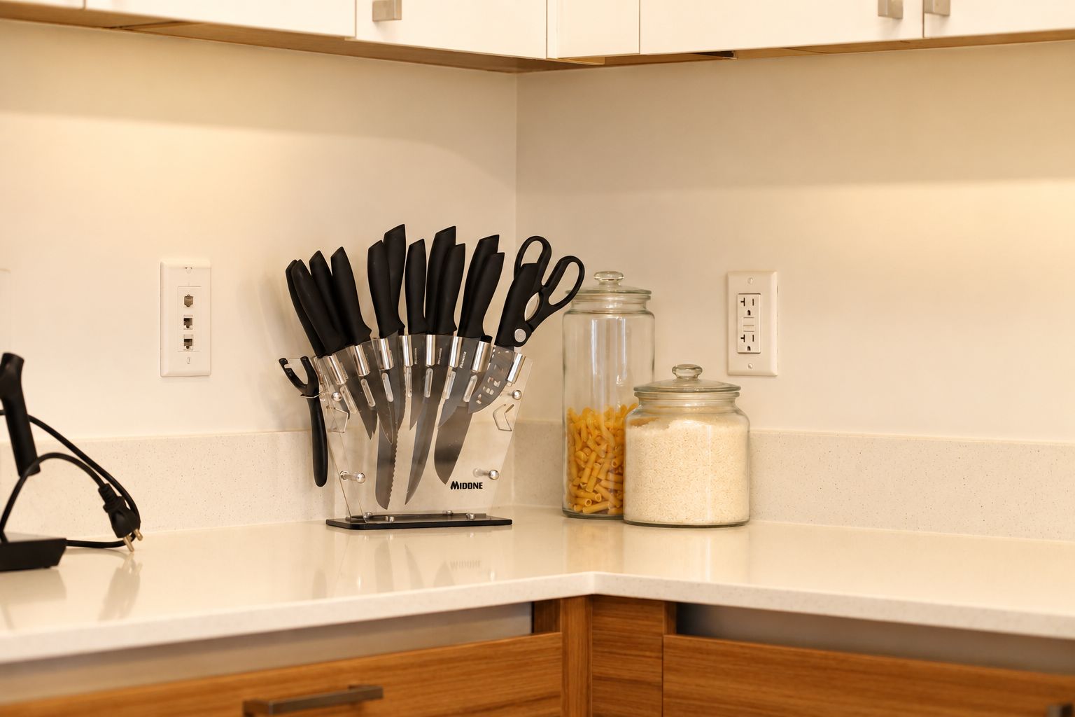 A kitchen counter with a knife block, a jar of pasta, and a jar of rice.