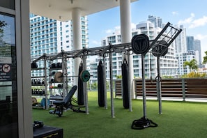 Ein Outdoor-Fitnessbereich mit Trainingsgeräten, einer Bank und Blick auf hohe Gebäude.