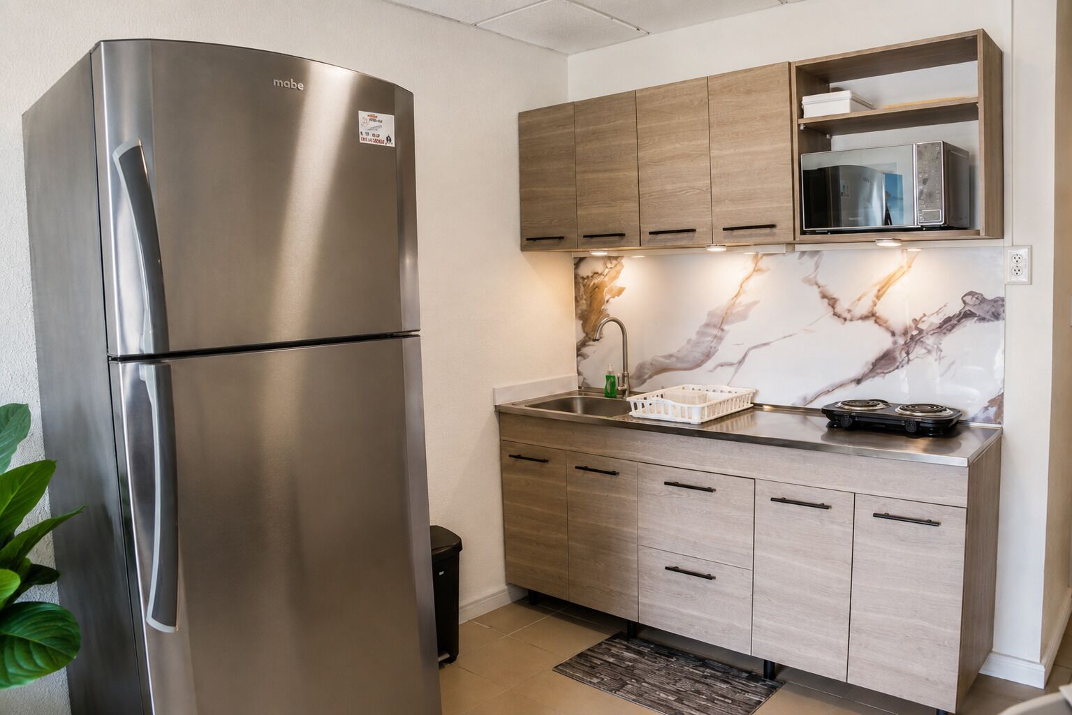 A modern kitchen with a stainless steel refrigerator, wooden cabinets, a marble backsplash, and a built-in microwave.