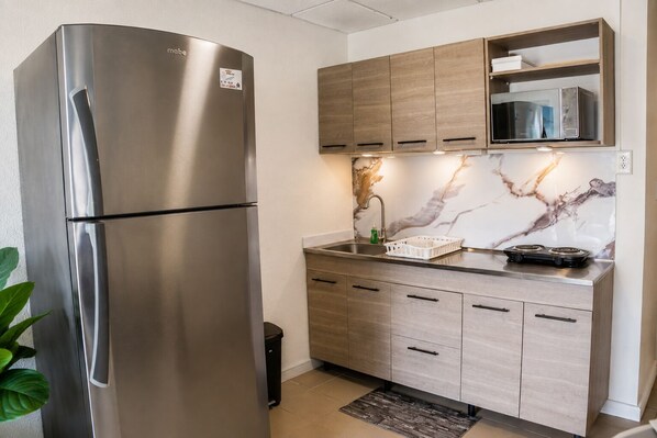 A modern kitchen with a stainless steel refrigerator, wooden cabinets, a marble backsplash, and a built-in microwave. - Charming 1-Bedroom Apartment In Vibrant Oranjestad (Oranjestad)
