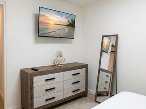 Un dormitorio con una cama, un aparador, un televisor montado en la pared y un espejo.