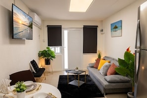 A living room with a sofa, a coffee table, a TV mounted on the wall, and a door with black blinds. - Charming 1-Bedroom Apartment In Vibrant Oranjestad (Oranjestad)