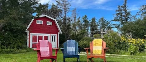 Una casa roja con tres sillas Adirondack en el frente, un césped y árboles al fondo.