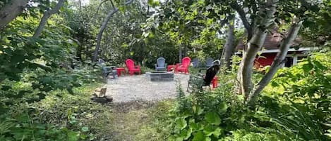 An outdoor seating area with red chairs and a fire pit surrounded by greenery.