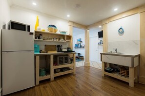 A compact kitchen with a refrigerator, microwave, wooden cabinets, and a sink. - Fisherman's Place - Anchor Down (Rocky Harbour)