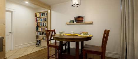 A dining area with a wooden table and chairs, a bookshelf, and a pendant light.