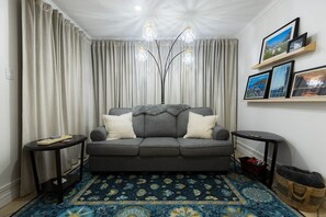 A living room with a grey sofa, two side tables, a patterned rug, a chandelier, and a wall with framed pictures.