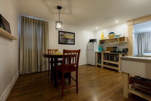 Een compacte keuken met een eettafel, stoelen, een koelkast en een spoelbak.