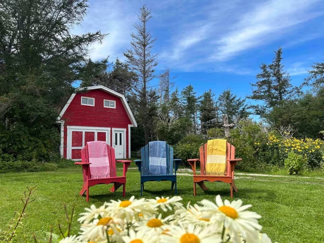 Una casa roja con tres sillas Adirondack en el frente, un césped y árboles al fondo.