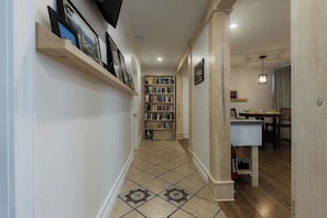 A hallway with a bookshelf, a dining area, and a kitchen.
