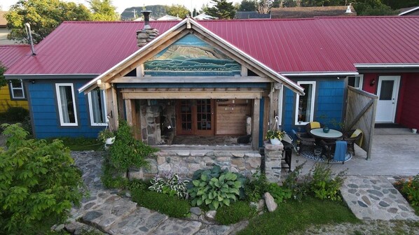 A building with a red roof, a stone foundation, and a front porch with a table and chairs.