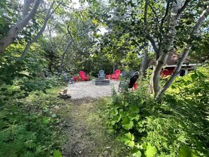 An outdoor seating area with red chairs and a fire pit surrounded by greenery. - Killick Place - Anchor Down (Rocky Harbour)