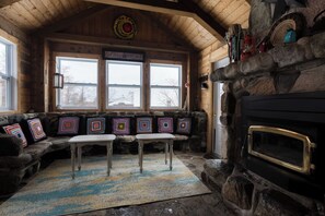 A cozy cabin interior with a stone fireplace, a bench with colorful cushions, and a stone wall.