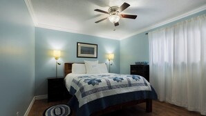 Un dormitorio con cama, dos lámparas de noche, un ventilador de techo, un cuadro enmarcado y una mesita de noche.
